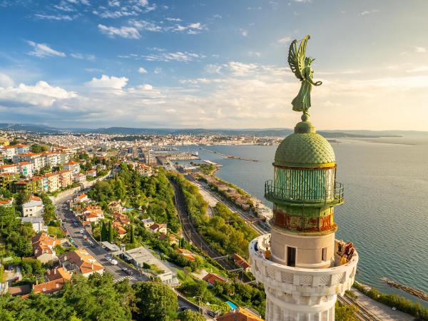 Faro della Vittoria lighthouse in Trieste city at sunny day, Italy. Aerial view of the cityscape of Trieste on Mediterranean sea coast in Italy. Historic lighthouse close-up